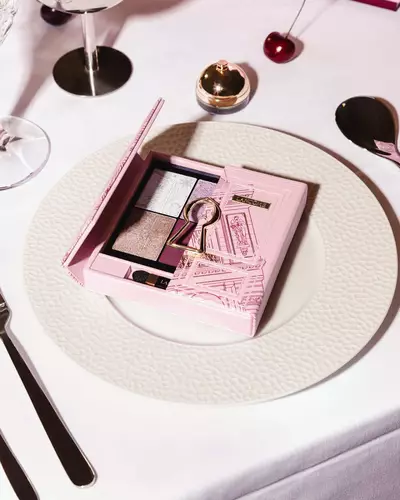 Ružičasta Lancome paleta sjenila za oči s motivom zlatne ključanice, elegantno servirana na bijelom svečanom tanjuru.