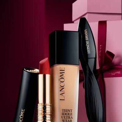 Elegantni slikovni prikaz Lancome L'Absolu Rouge mat ruža za usne, Teint Idole Ultra Wear tekućeg pudera i Hypnose Drama maskare na luksuznoj tamnocrvenoj blagdanskoj pozadini.