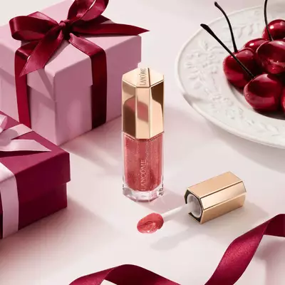 Lancome sjajilo za usne u nijansi bobičastog voća u luksuznoj šesterokutnoj bočici, stilizirano s poklon-kutijama i trešnjama.