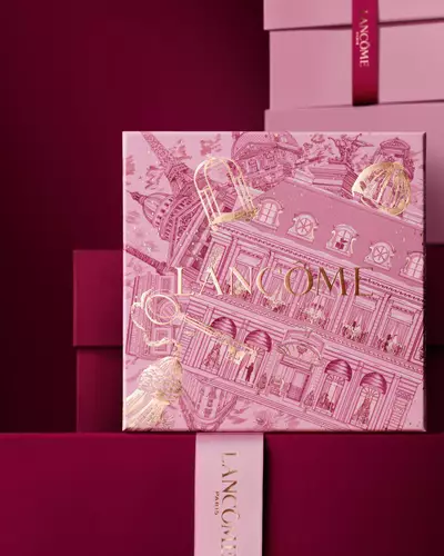 Slika ružičaste Lancome blagdanske poklon kutije ispred niza ružičastih i tamnocrvenih kutija na tamnocrvenoj pozadini.