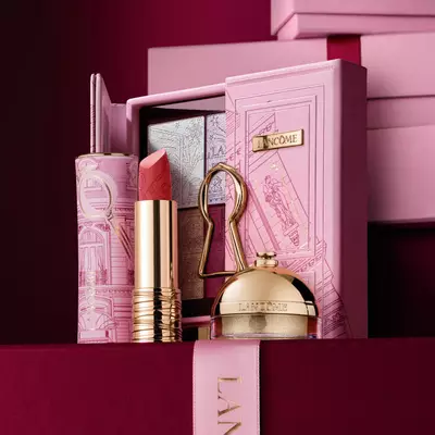 Raskošan Lancome blagdanski poklon set koji uključuje ruž za usne, paletu sjenila i zlatne proizvode za uljepšavanje, izložen uz ukrasnu ružičastu kutiju.