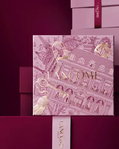 Ružičasta Lancome bočica parfema stilizirana na svijetloj površini s poklon-kutijom, vrpcom i crvenim ribizom.