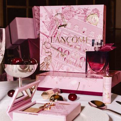 Svečano predstavljanje Lancome blagdanske linije na stolu s velikom ružičastom ilustriranom kutijom, parfemom, makeup proizvodima i svježim trešnjama.