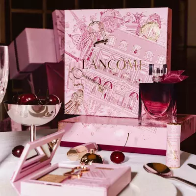 Svečano predstavljanje Lancome blagdanske linije na stolu s velikom ružičastom ilustriranom kutijom, parfemom, makeup proizvodima i svježim trešnjama.