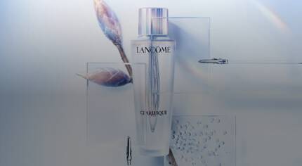 Boca seruma Lancome Clarifique s prozirnom etiketa, okružena ilustracijom cvjetnih pupova i mjehurića vode.