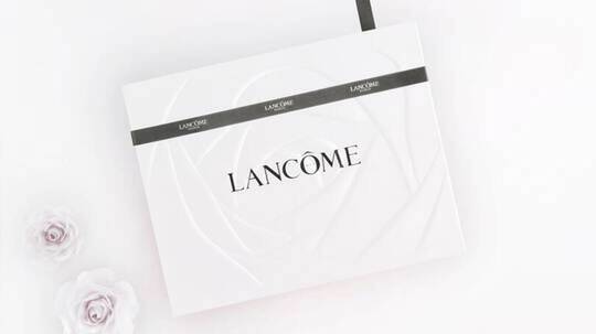 Elegantna bijela kutija s natpisom 'Lancome', ukrašena tamnozelenom vrpcom i sitnim ružama.