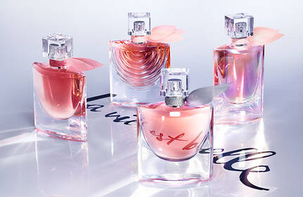 Four elegant perfume bottles are arranged on a light background, with soft pink and floral accents. The scene is bright and sophisticated, conveying a sense of luxury and allure.