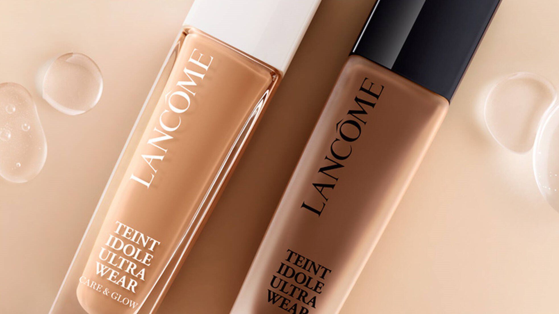 Alt tekst: Dva bočica tekućeg pudera Lancome Teint Idole Ultra Wear na svijetloj pozadini, s nekoliko kapljica vode oko njih.