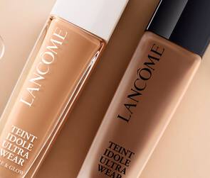 Alt tekst: Dva bočica tekućeg pudera Lancome Teint Idole Ultra Wear na svijetloj pozadini, s nekoliko kapljica vode oko njih.
