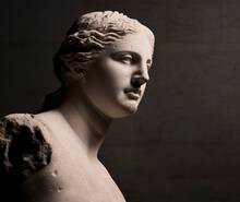 A close-up view of a marble statue of a woman's head and shoulders, featuring classical details and softly illuminated to emphasize its texture and form.