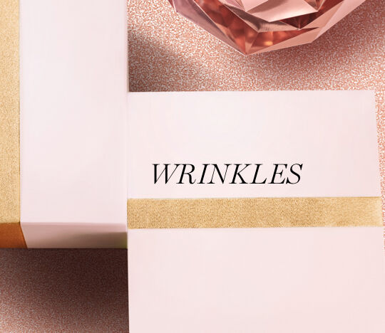 A close-up of pink boxes with gold stripes, featuring the word "WRINKLES" in elegant black font, set against a textured background.