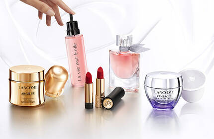 A display of various beauty products, including a moisturizer, a pink spray, a perfume, lipstick, and a cream, arranged elegantly on a light background.