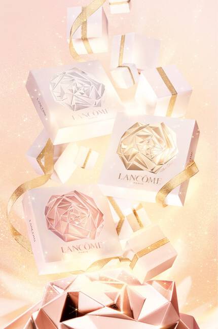 A festive scene featuring elegantly wrapped gifts from Lancome, surrounded by sparkling confetti and shimmering ribbons against a soft pink background.