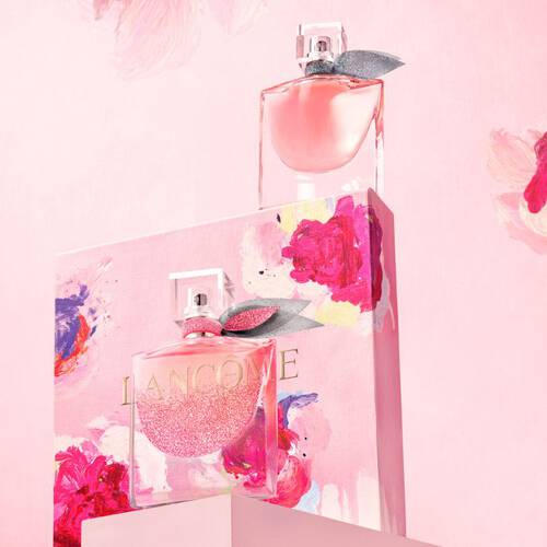 Two elegant perfume bottles are displayed atop a beautifully decorated box featuring vibrant pink and floral designs. The background is a soft pink, enhancing the overall romantic aesthetic.