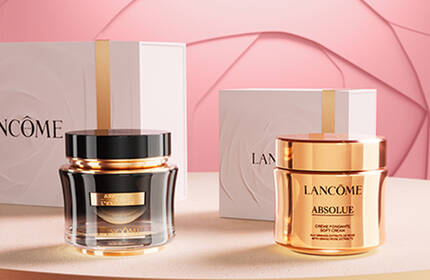 A display of luxurious Lancome skincare products, including a black jar and a gold jar, situated on a light pink background with elegant packaging.