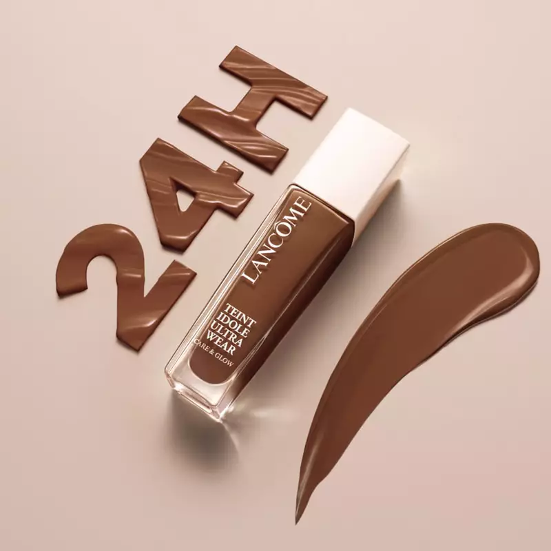 A bottle of Lancome foundation in a deep brown shade, with a swatch of the product beside it and the text "24H" made from chocolate-colored material in the background.