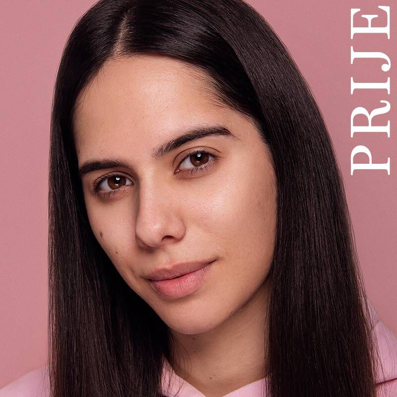 Žena s dugom tamnom kosom gleda u kameru, uz blagi osmijeh, na pozadini u nijansi svijetle ružičaste boje. Sa strane se nalazi natpis "PRIJЕ".