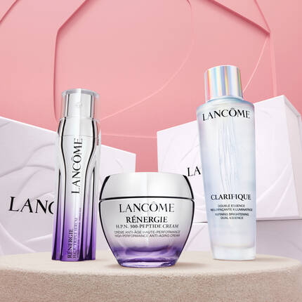Tri proizvoda za njegu kože marke Lancome na pastelnoj pozadini: bočica s tekućim serumom, anti-aging kremom i dvostrukim esencijalnim tonikom.
